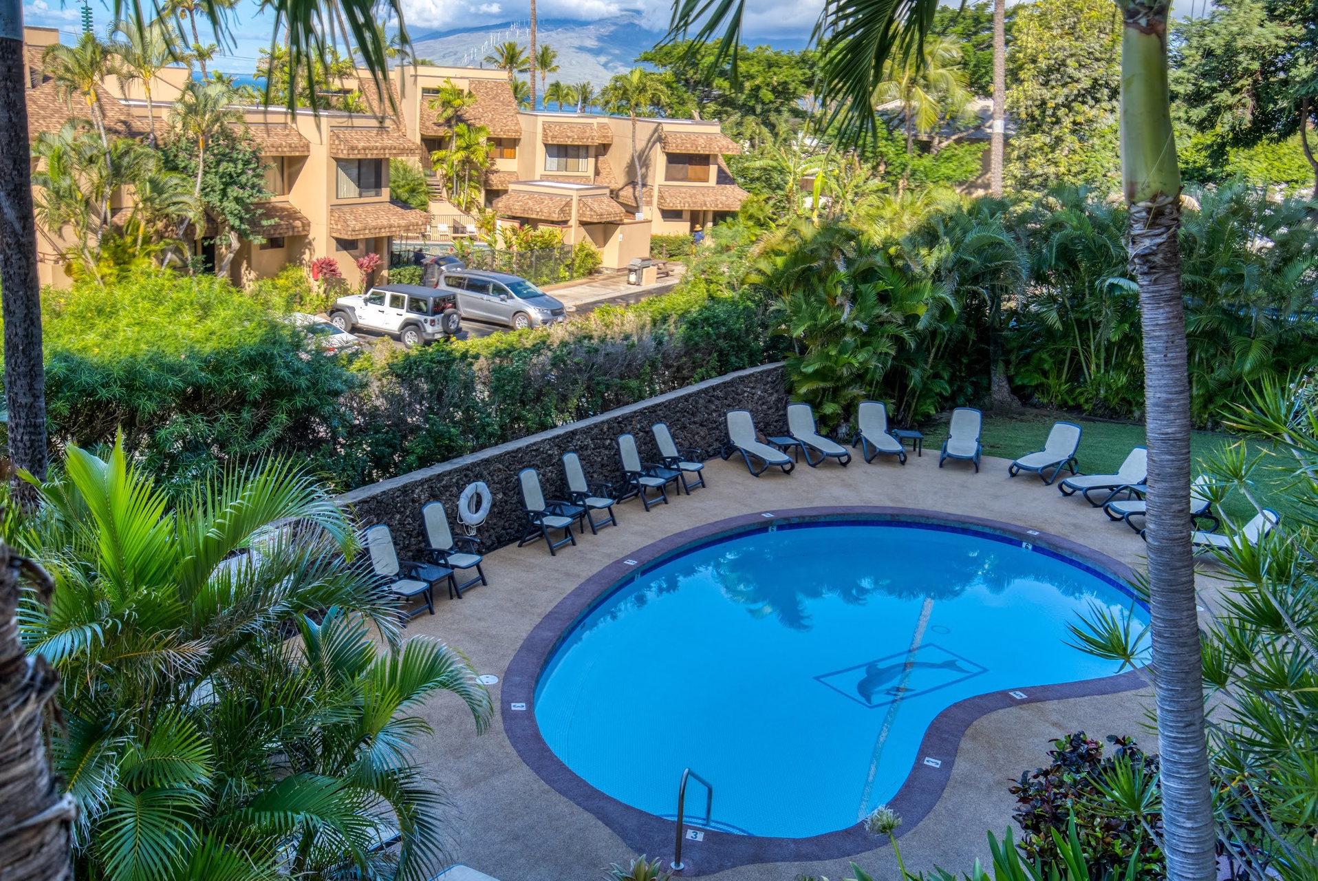 Elevated view showcasing the property's outdoor pool area, landscaped grounds with lush tropical palms, and multi-level building structures nestled among greenery. The resort features convenient parking and scenic natural surroundings.
