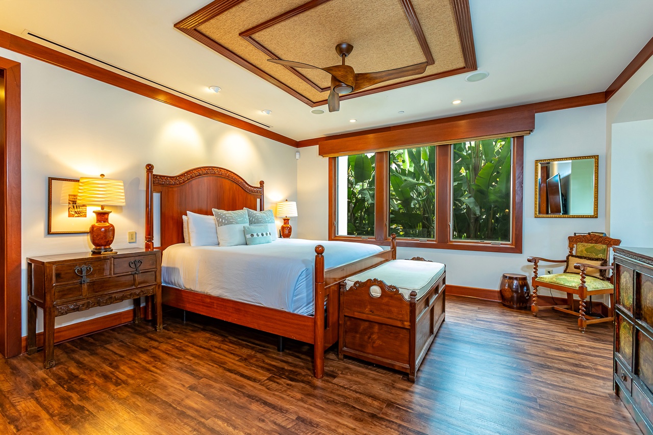 Your sanctuary awaits with elegant wood finishes, a plush bed beneath a decorative tray ceiling, and lush tropical greenery framed by your windows—your peaceful retreat surrounded by nature.