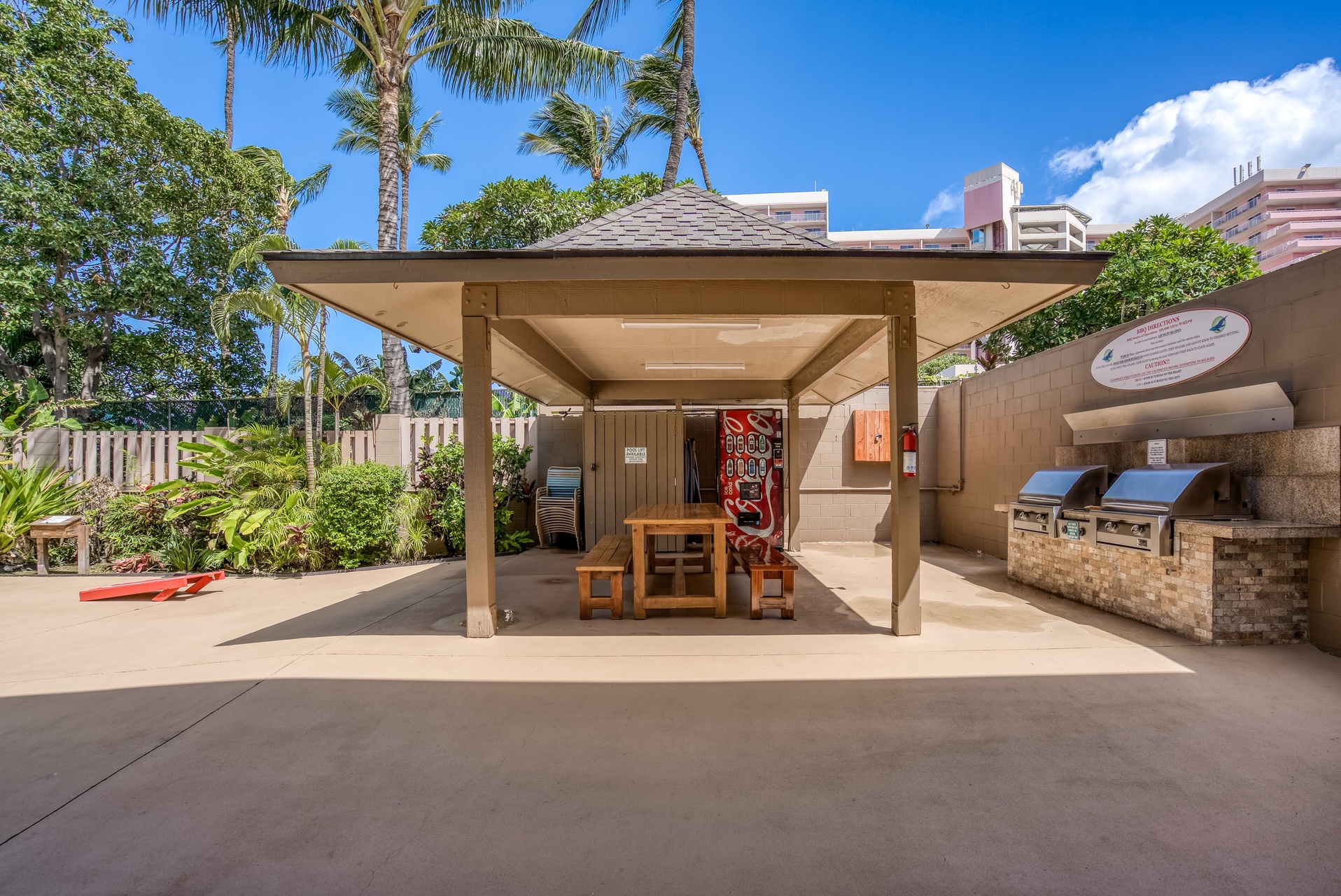 The property features an outdoor BBQ pavilion with built-in grills and a dining table, set amidst tropical gardens and lush palm trees.