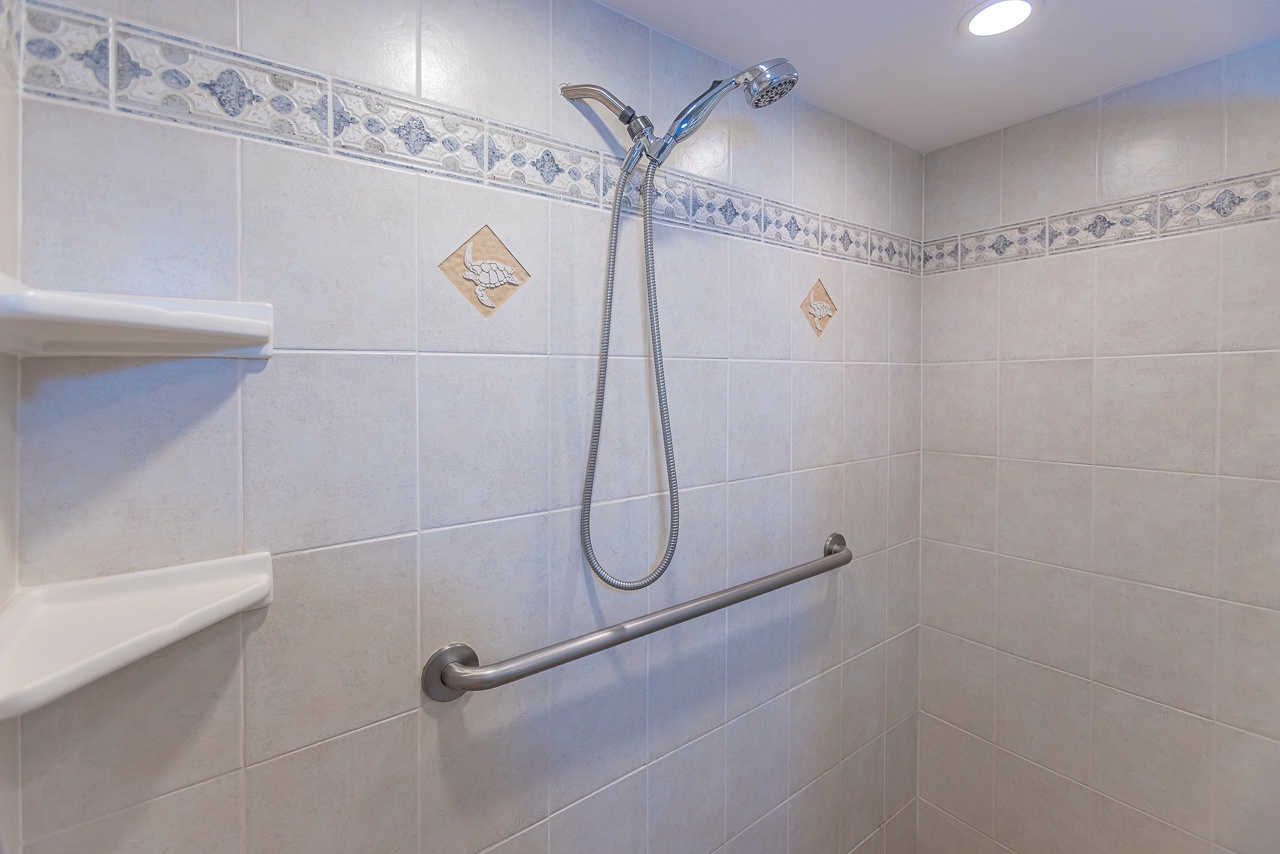 This accessible bathroom features a walk-in shower with dual showerheads, a safety grab bar, built-in shelf, and elegant tiled design for your comfort.