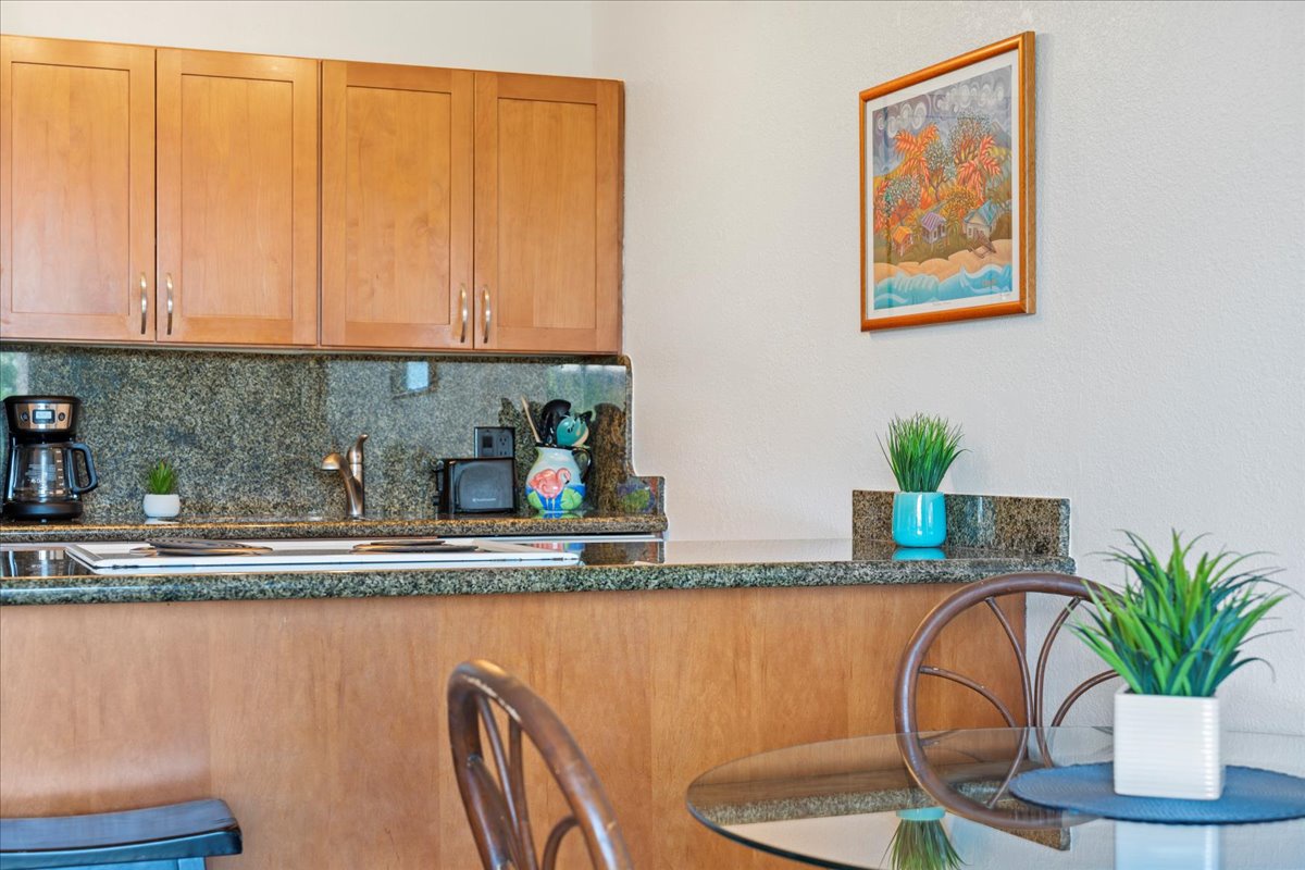 Your open kitchen and dining area invites easy, relaxed meals with warm wood tones and granite counters. Sip your morning coffee at the glass table, surrounded by touches of green and coastal charm.