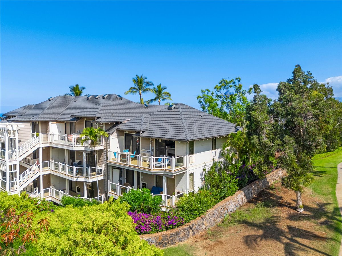 Multi-level property with balconies surrounded by lush tropical landscaping, palm trees, and vibrant flowering plants under a clear blue sky in a serene resort setting.