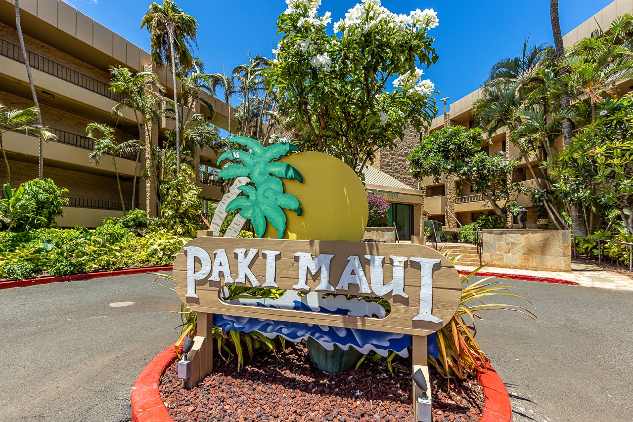 The distinctive 'Paki Maui' sign welcomes arrivals under the bright Hawaiian sun, framed by tropical landscaping and palm trees that define the property's entrance and island setting.