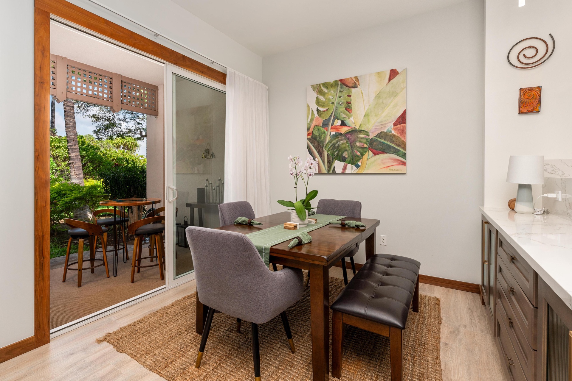 Gather around your elegant dining table where tropical artwork and natural light create the perfect setting for memorable meals together.