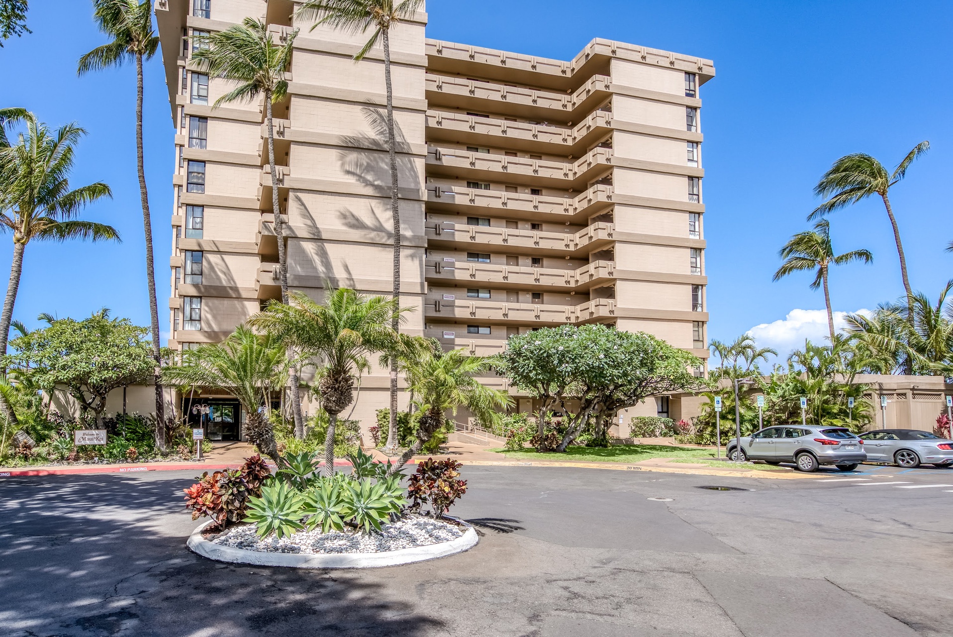 Tropical beachfront condo building surrounded by lush landscaping and swaying palms, offering the ultimate Hawaiian getaway.