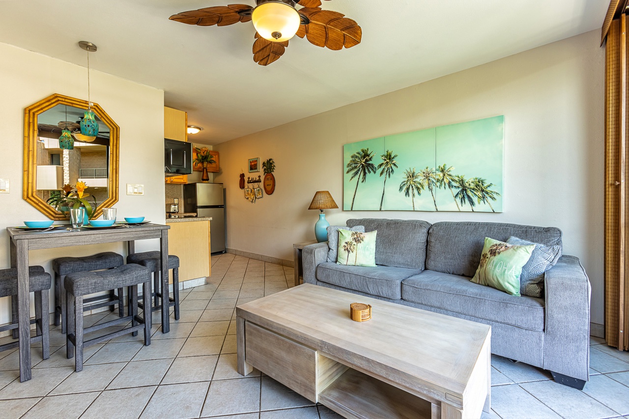 Your bright, tropical-inspired living space features coastal charm with breezy ceiling fan, comfortable seating, and an open flow to the kitchen.