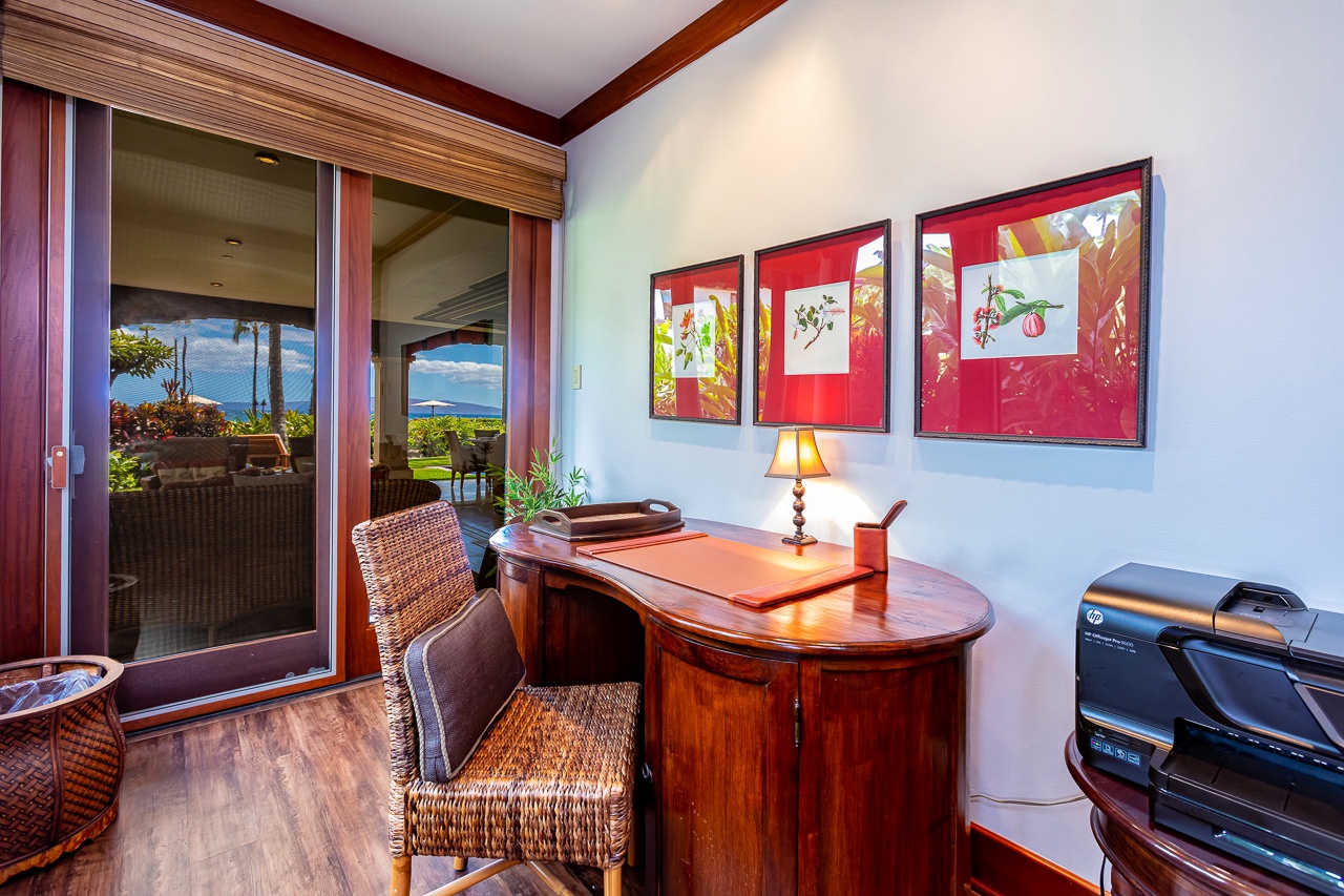 Step through the sliding doors and discover your personal workspace with a polished desk, woven chair, and vibrant tropical artwork—all with glimpses of lush greenery and ocean beyond.
