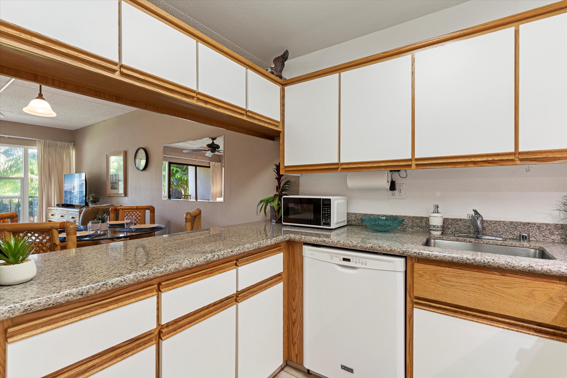 Your fully equipped kitchen invites you to prepare meals with ease, featuring ample counter space, modern appliances, and natural light streaming through the open living area beyond.
