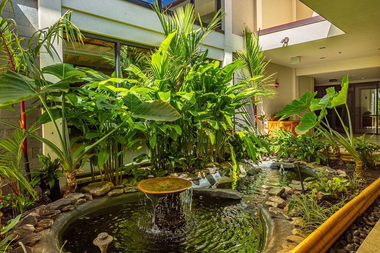 A serene indoor courtyard greets visitors with lush tropical plantings, a trickling fountain, and natural stone accents that set a tranquil tone for your arrival.