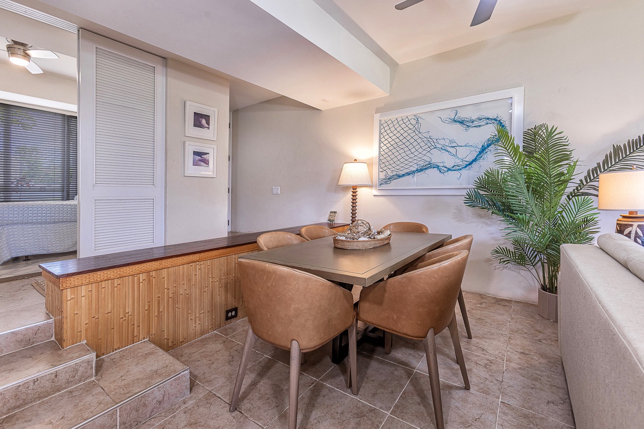 Gather around this inviting dining table where coastal charm meets modern comfort. Warm leather chairs, nautical art, and lush tropical touches create your perfect space for memorable meals.