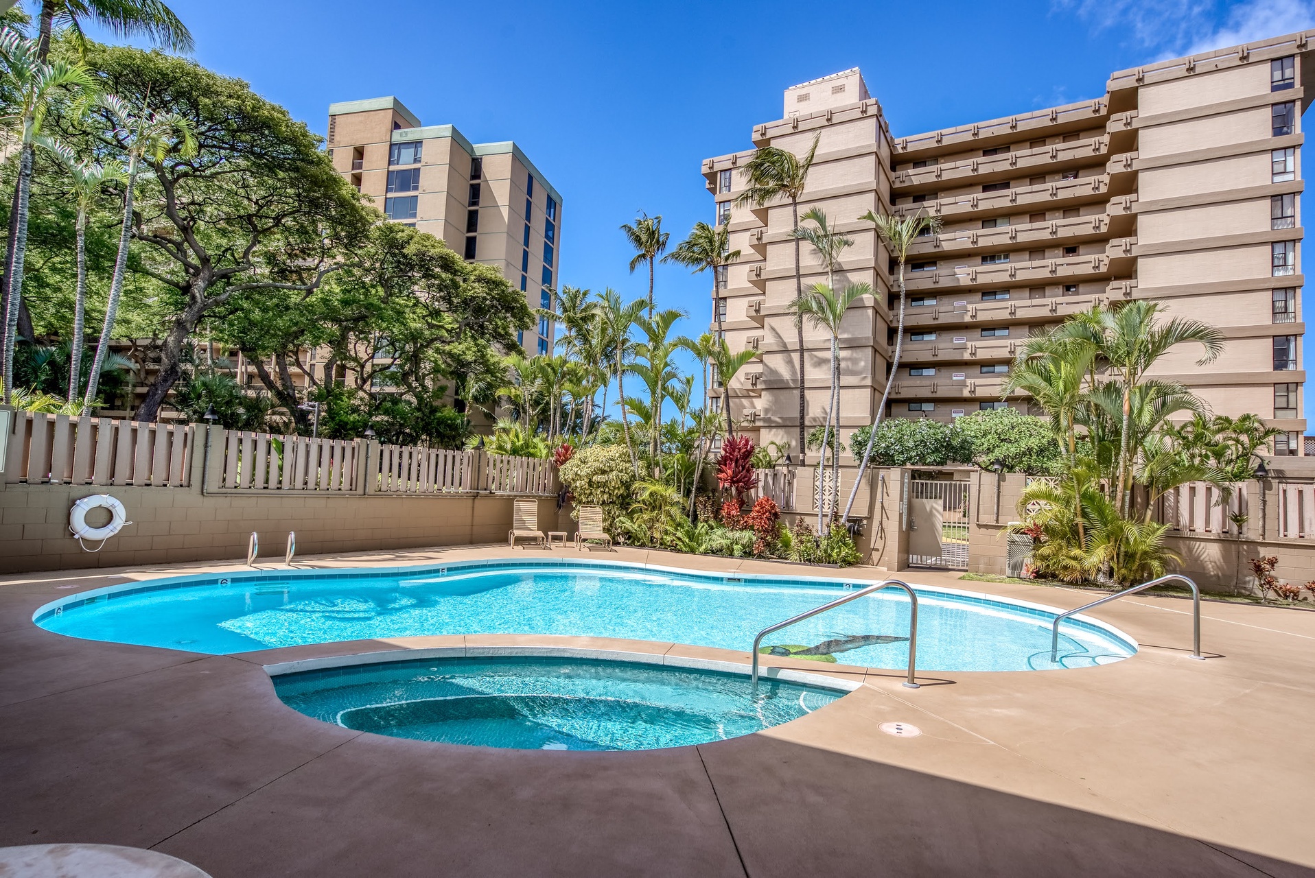 The property features a refreshing outdoor pool and hot tub nestled among tropical landscaping, with palm trees and lush greenery creating a relaxing resort atmosphere.