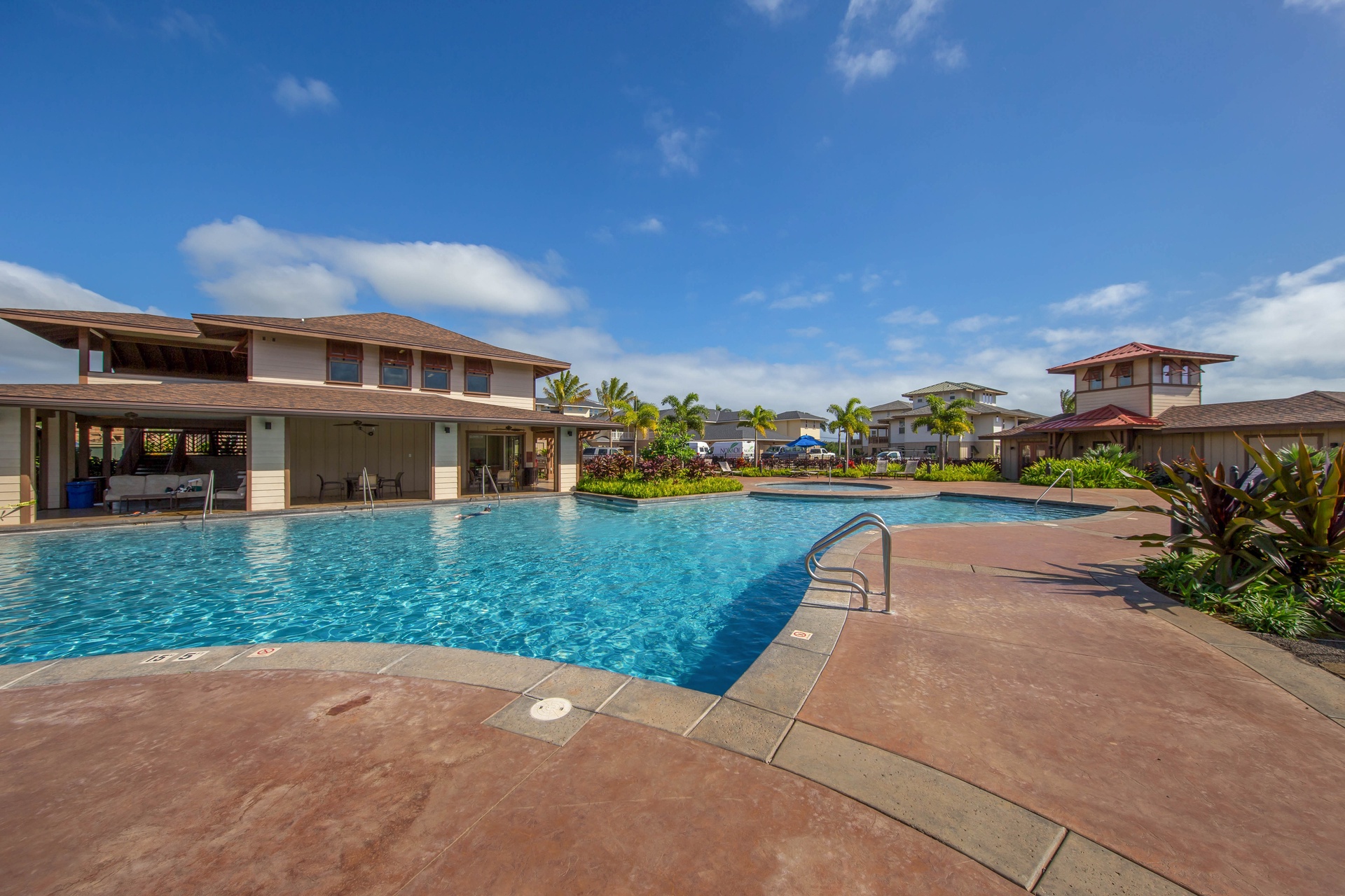 Sparkling swimming pool with tropical palm trees and modern clubhouse facilities set against blue Hawaiian skies.