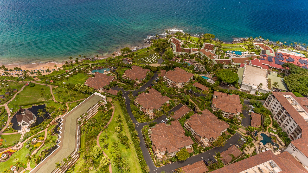 An aerial view captures the oceanfront resort nestled along turquoise waters, showcasing lush tropical grounds, swimming pools, and beachfront access in a stunning coastal setting.