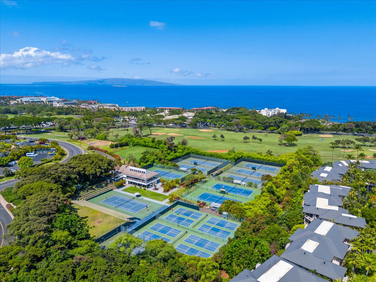 Aerial view of the resort complex showcasing tennis courts, golf course, and oceanfront surroundings in a lush coastal setting with mountain vistas.