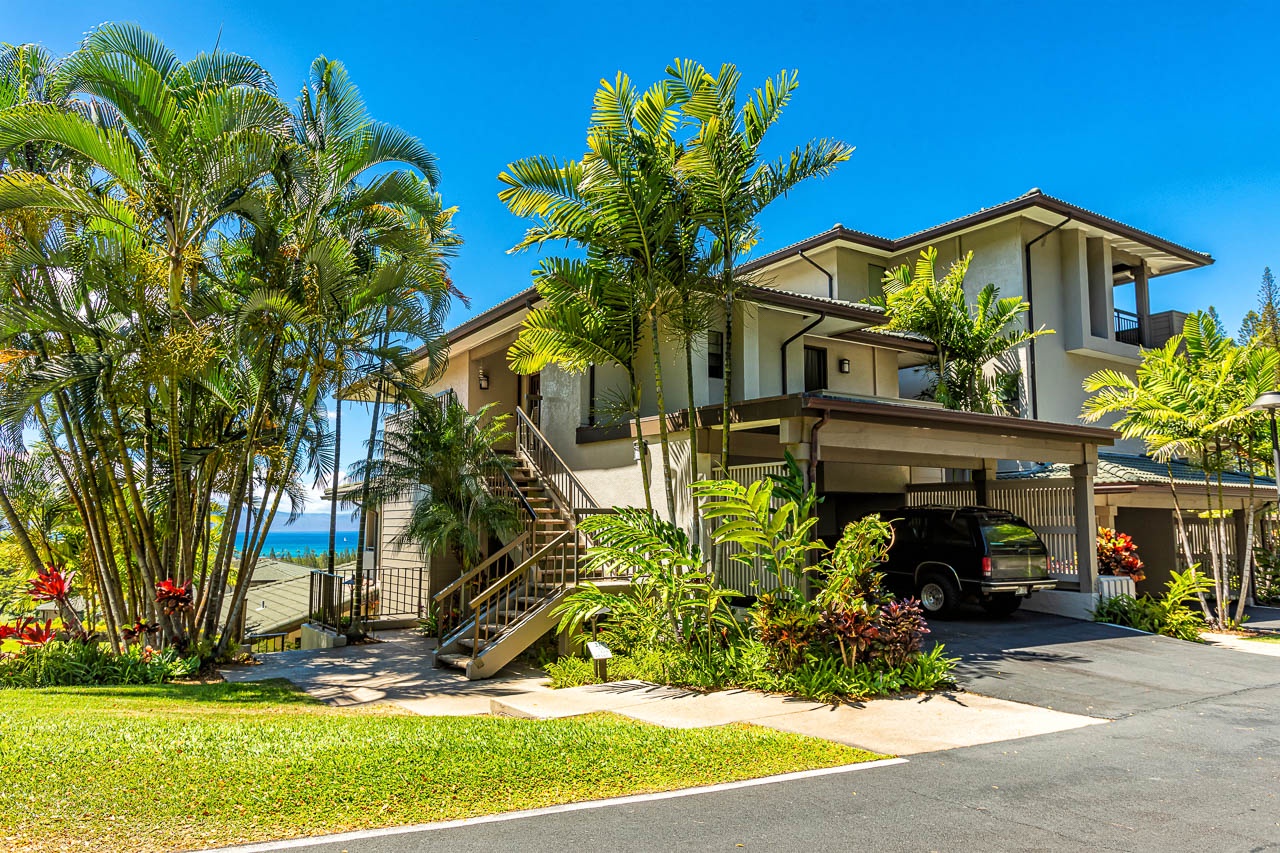 A tropical two-story villa with expansive balconies, lush landscaping, and covered parking, set in a sun-drenched coastal neighborhood with ocean views.