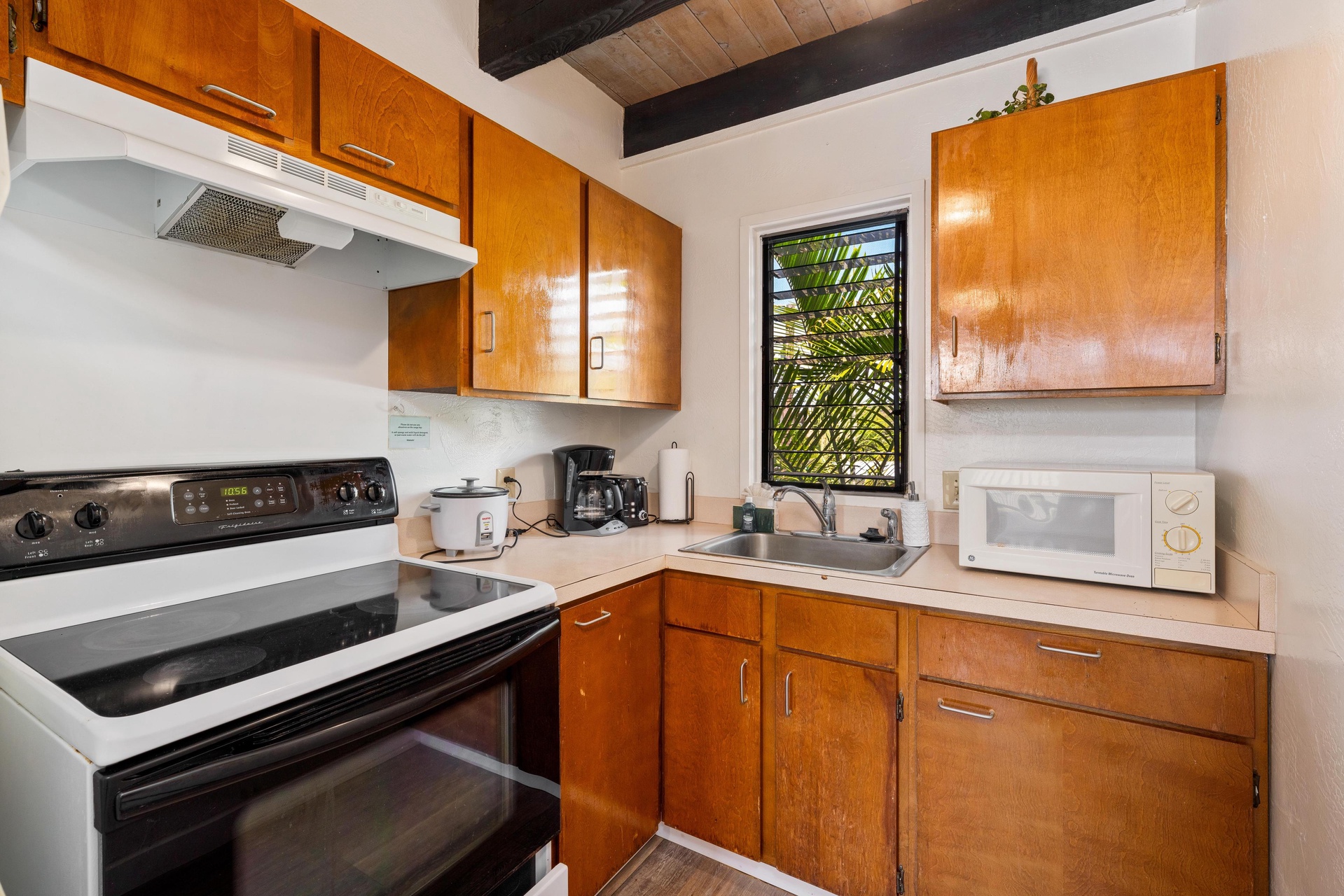 A fully equipped kitchen with warm wood cabinets, stove, microwave, and coffee maker—everything you need to prepare your favorite meals while enjoying tropical views through the window.