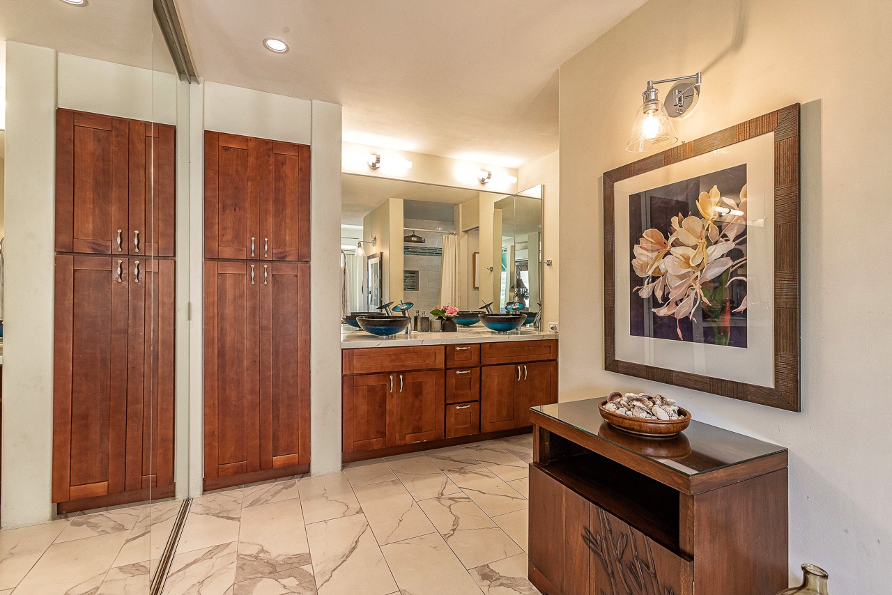 Your private bathroom sanctuary features elegant marble floors, custom wood cabinetry, dual vessel sinks, and art-adorned walls—a luxurious space designed for comfort and style.