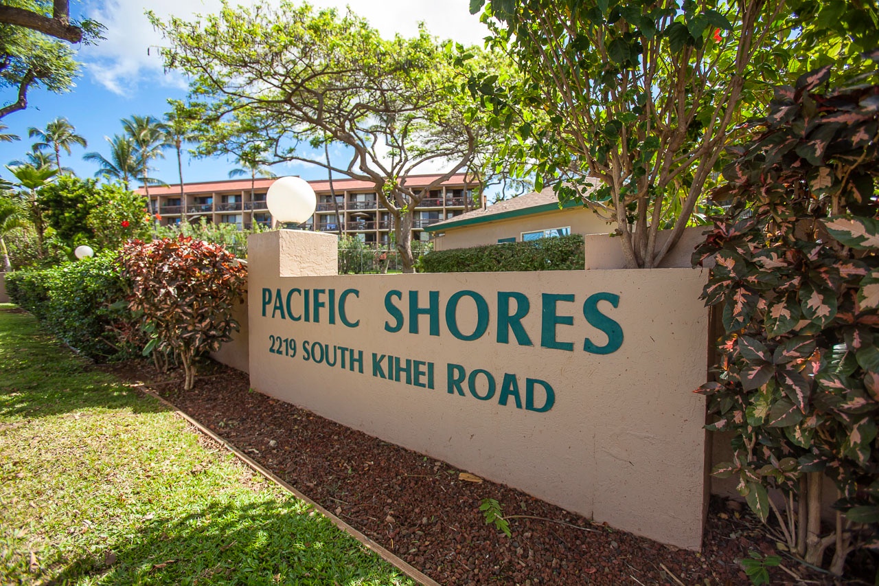Pacific Shores property entrance sign welcomes visitors to this tropical Kihei location, surrounded by lush landscaping and palm trees.