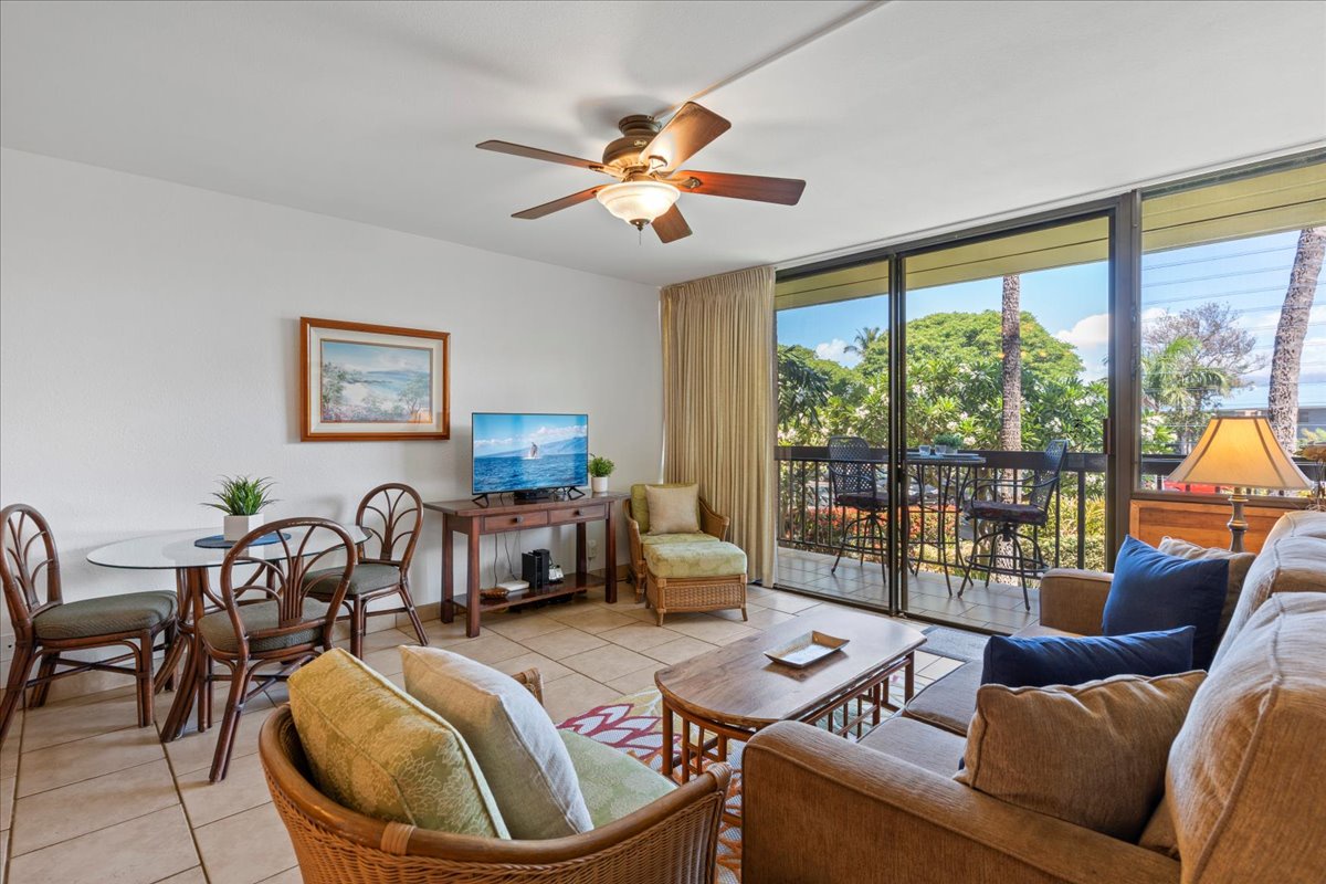 Step into your bright, island-inspired living space where a gentle breeze from the ceiling fan and the lush tropical greenery visible through your balcony doors create the perfect Hawaiian escape.