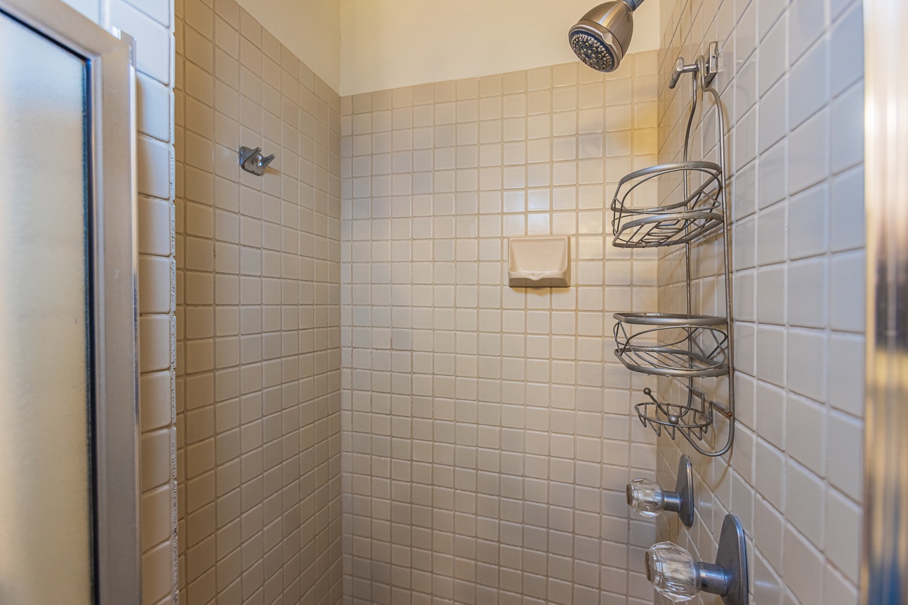 Your private shower sanctuary with gleaming white tiles, chrome fixtures, and convenient storage caddies for all your essentials.