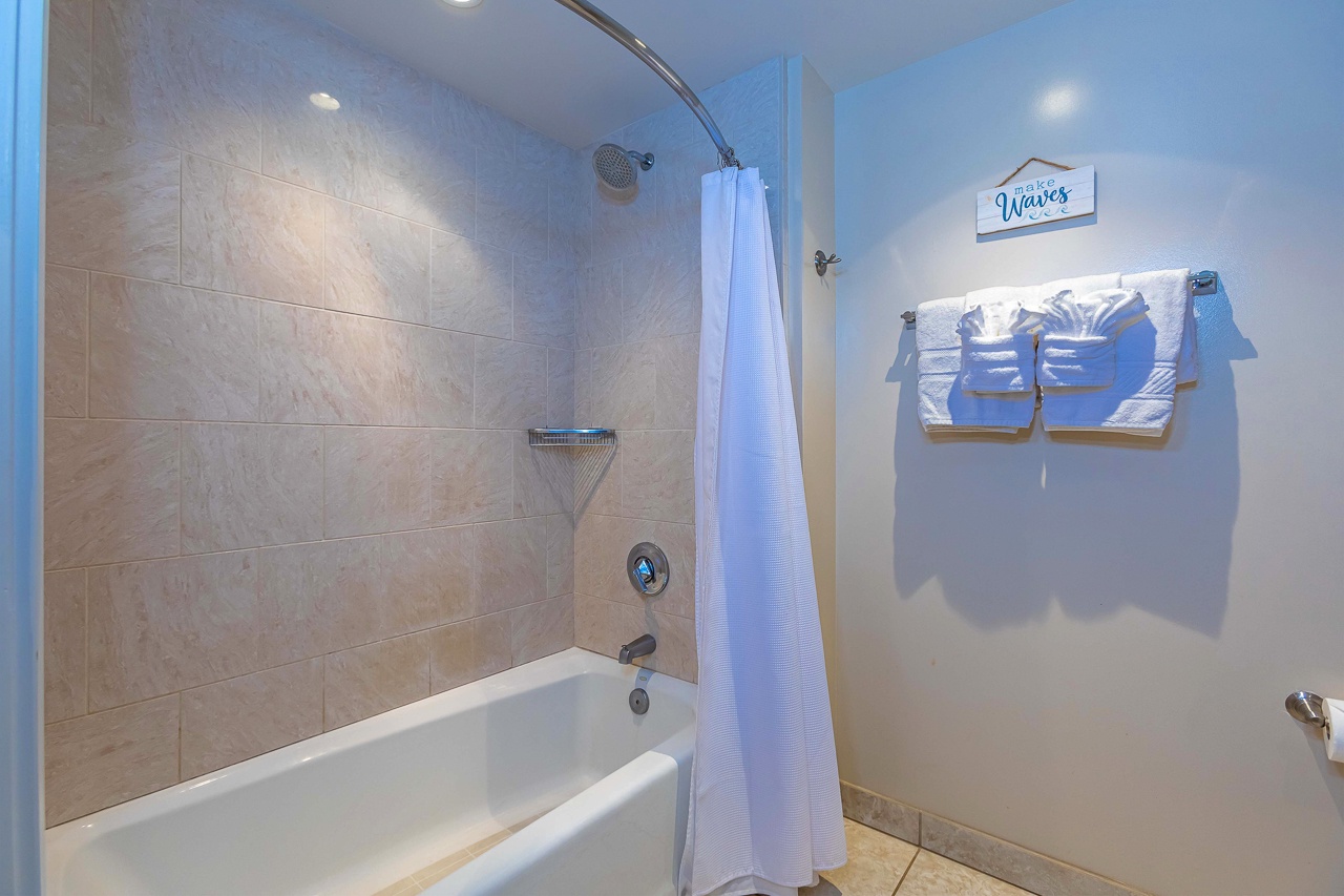 Your bright coastal bathroom features a full tub-shower combo with gleaming tile surround, fresh towels, and beachy decor.