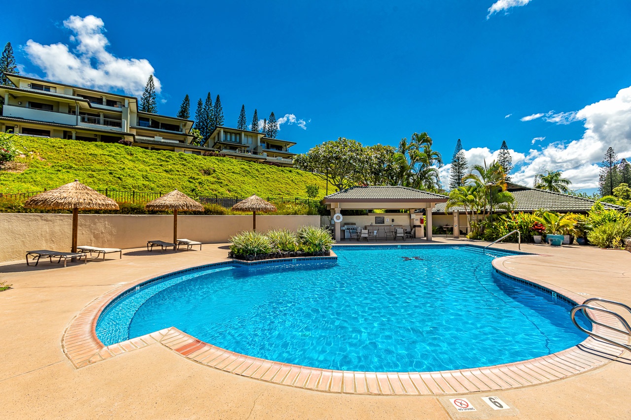A sparkling blue pool surrounded by lush tropical landscaping, thatched umbrellas, and sunny lounging areas awaits you under beautiful Hawaiian skies.