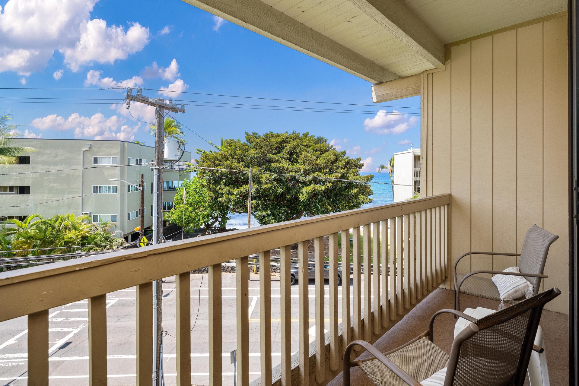 Balcony overlooks a partial ocean view framed by lush greenery, offering a quiet spot to enjoy the coastal setting and island scenery beyond.