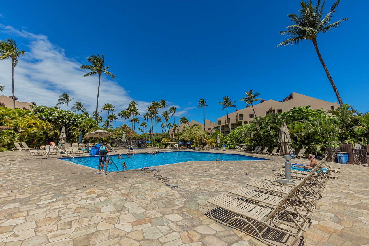 A spacious pool deck framed by swaying palms and tropical greenery, where your days begin with sunshine and end with island breezes—your perfect Hawaiian escape.