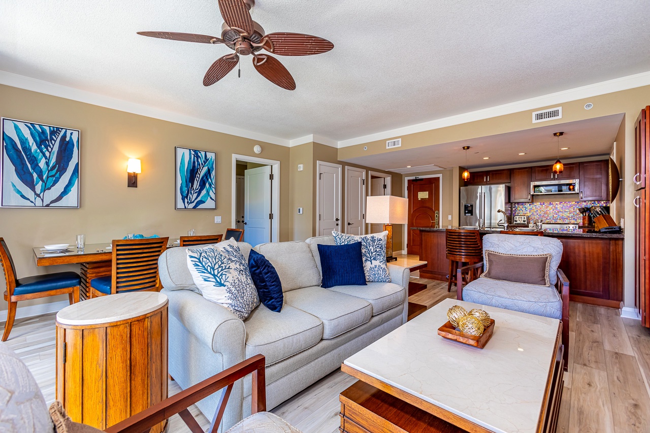 Sink into plush seating and warm tropical tones in your open-concept living space, where coastal artwork and rich wood accents welcome you home after a day exploring paradise.