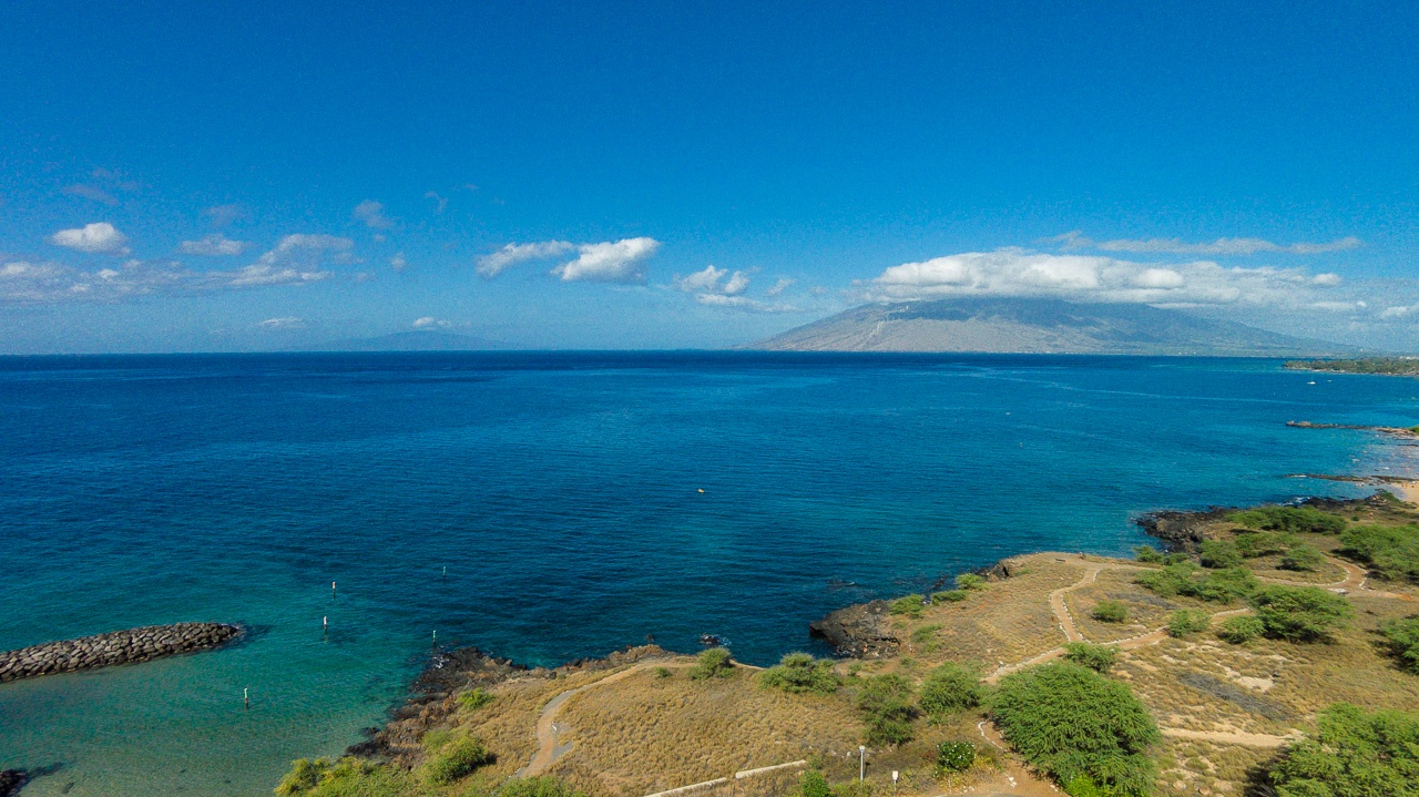 Stunning aerial view showcases the pristine coastline with turquoise waters and distant mountain silhouette creating a breathtaking tropical paradise backdrop.