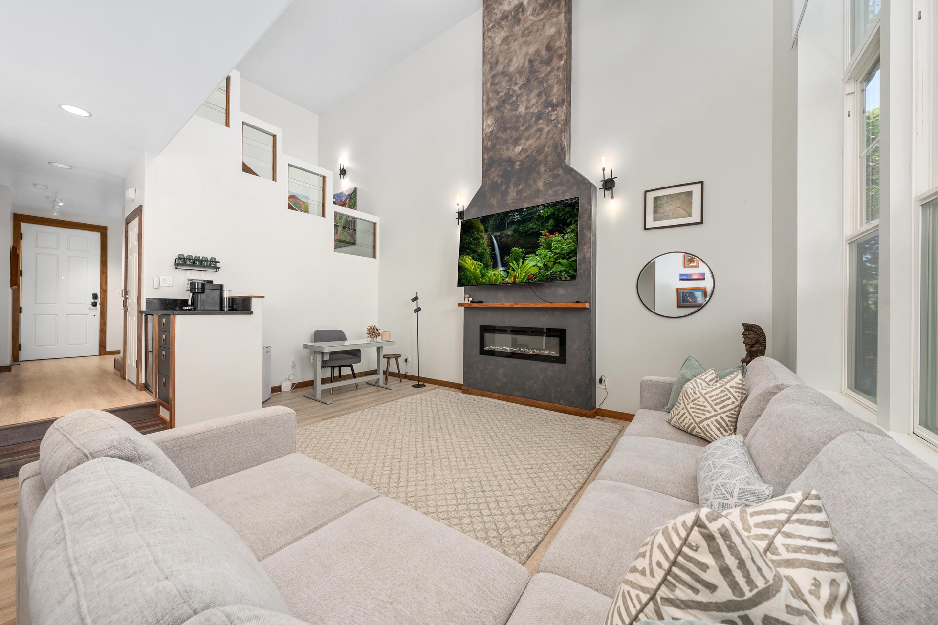 Sink into plush sofas by the striking stone fireplace, where natural light streams through tall windows and modern comfort meets elegant design.