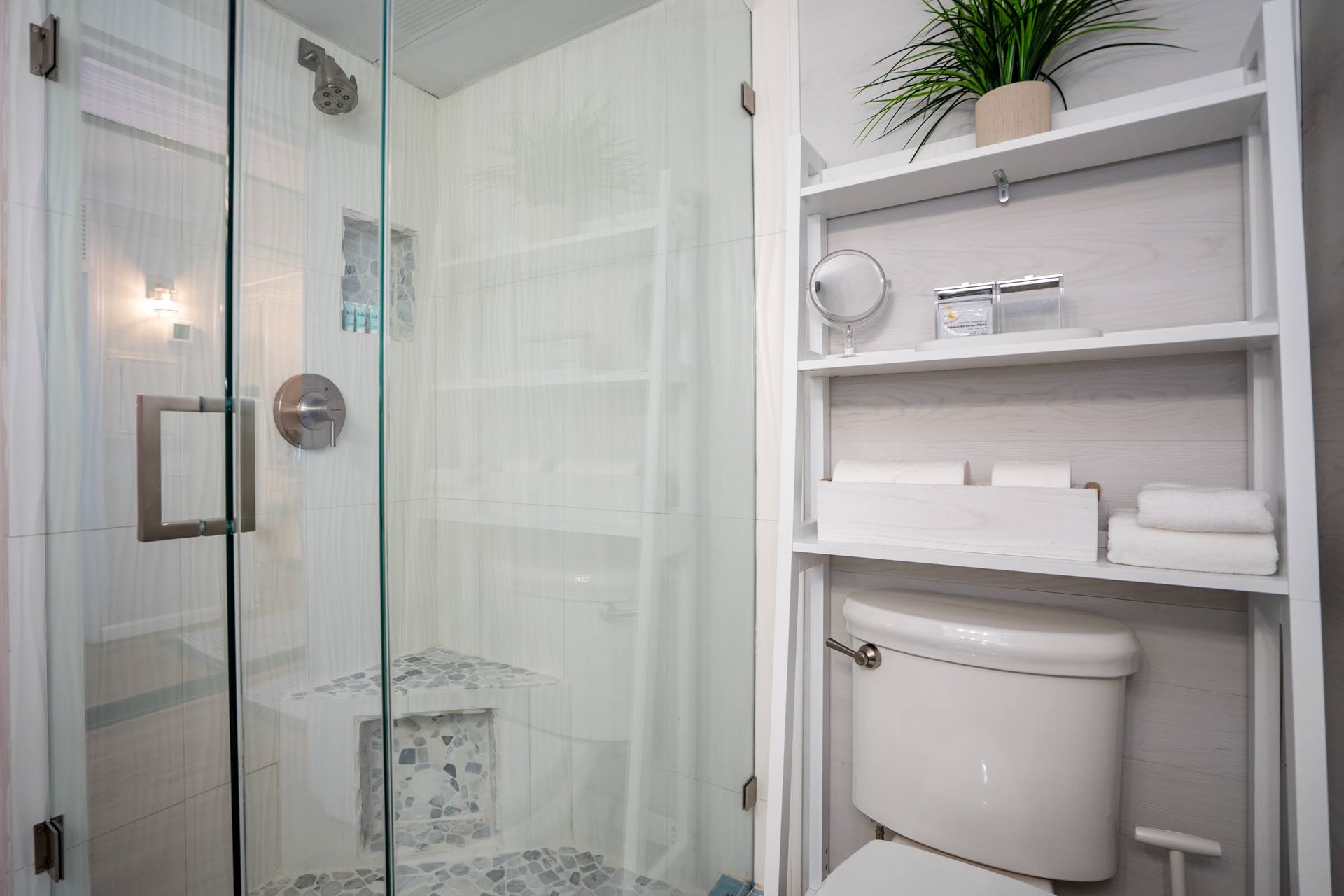 Step into your sleek, spa-like bathroom featuring a spacious walk-in shower with beautiful pebble tile flooring and crisp white finishes. Fresh towels await on open shelving for your convenience.