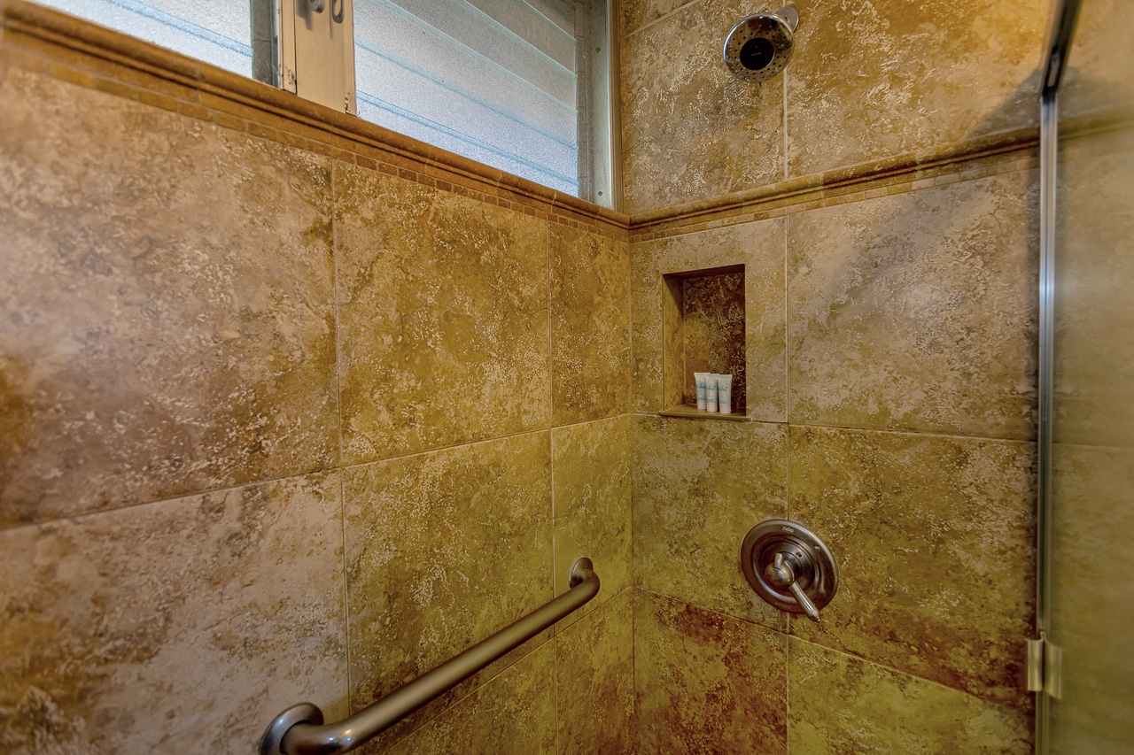 Your private shower features warm stone-effect tiles, a built-in niche for toiletries, natural light from above, and a safety grab bar for added comfort and peace of mind.