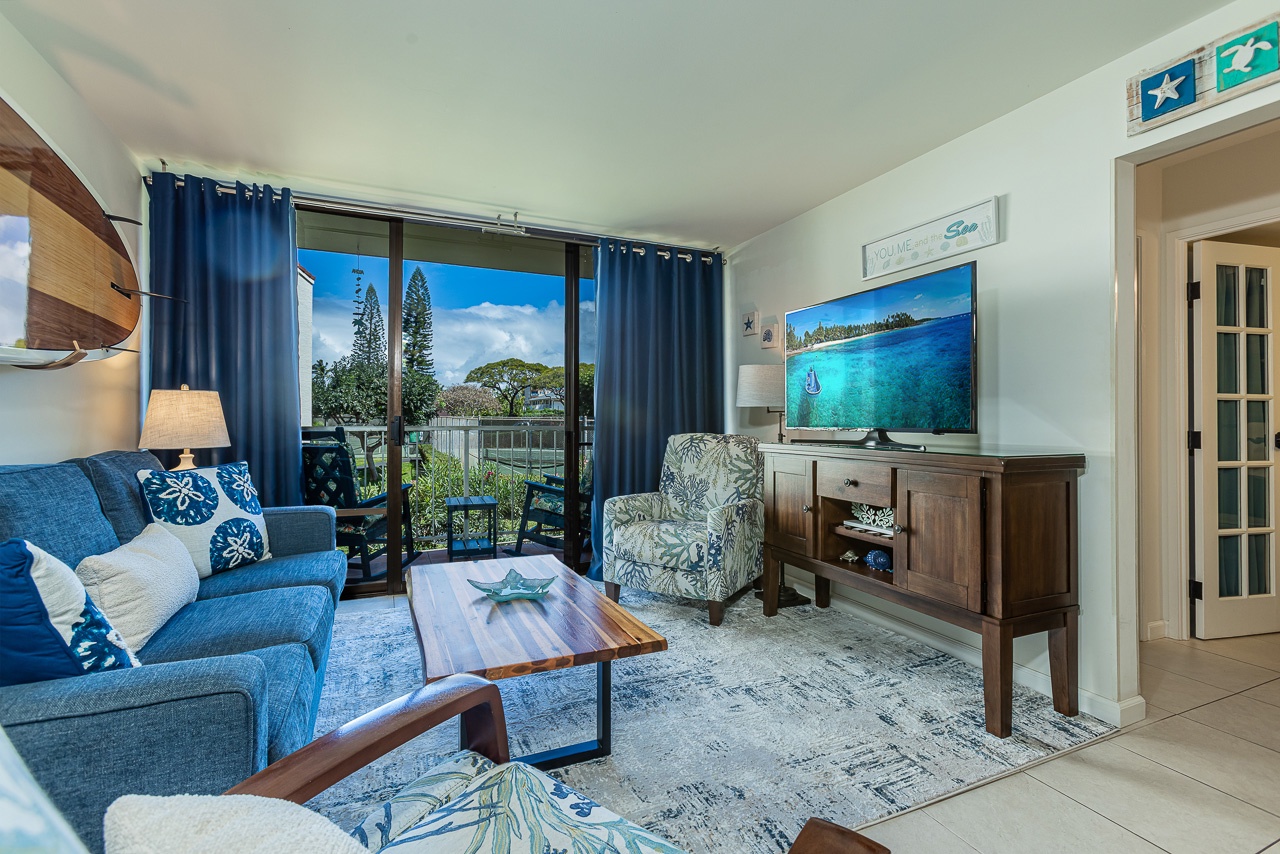 Your bright living space features coastal-inspired décor with plush blue seating and garden views through sliding doors.