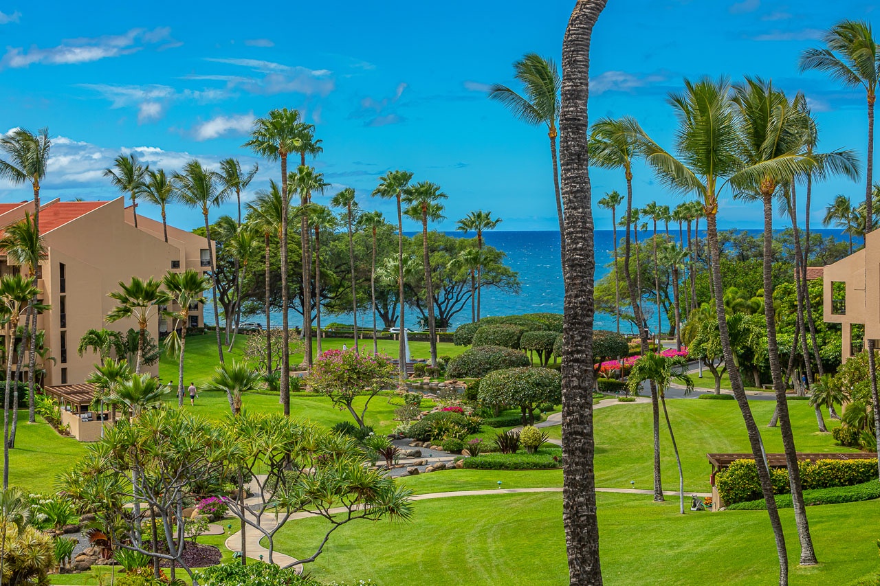 The property offers lush tropical grounds with towering palms, vibrant gardens, and sweeping views of the sparkling blue Pacific Ocean just beyond.