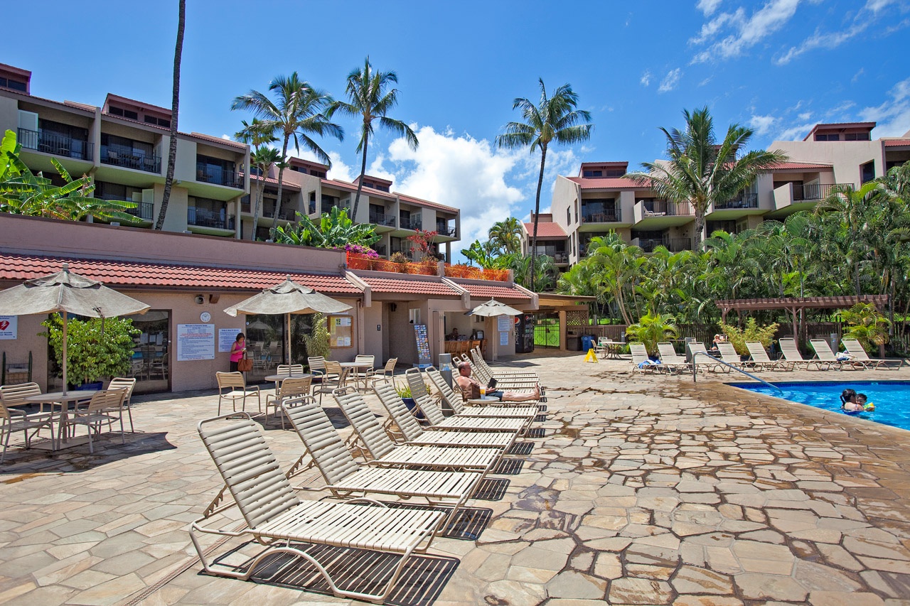 The property features outdoor pool facilities surrounded by tropical landscaping and resort-style lounge areas under sunny Hawaiian skies.