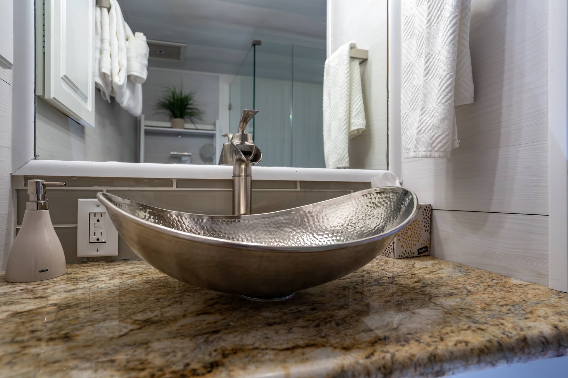 The hammered metal vessel sink adds artisan elegance to your bathroom, paired with luxurious granite countertops and plush white towels at the ready.