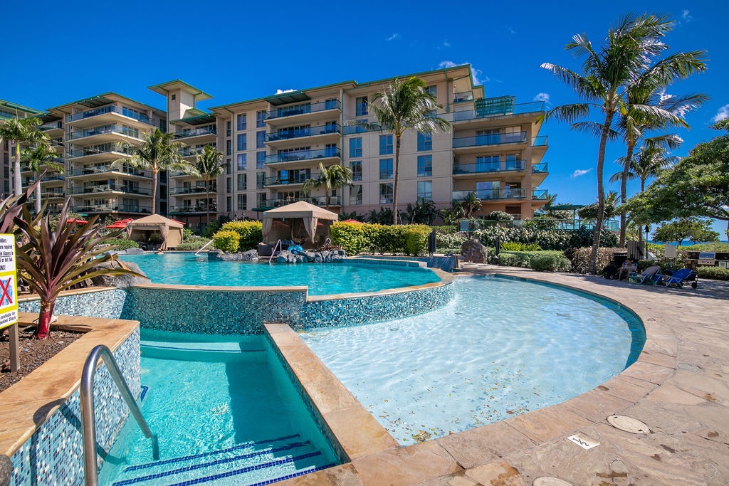 The building rises against a bright blue sky, surrounded by swaying palms and an inviting multi-level pool area—your perfect tropical retreat awaits.
