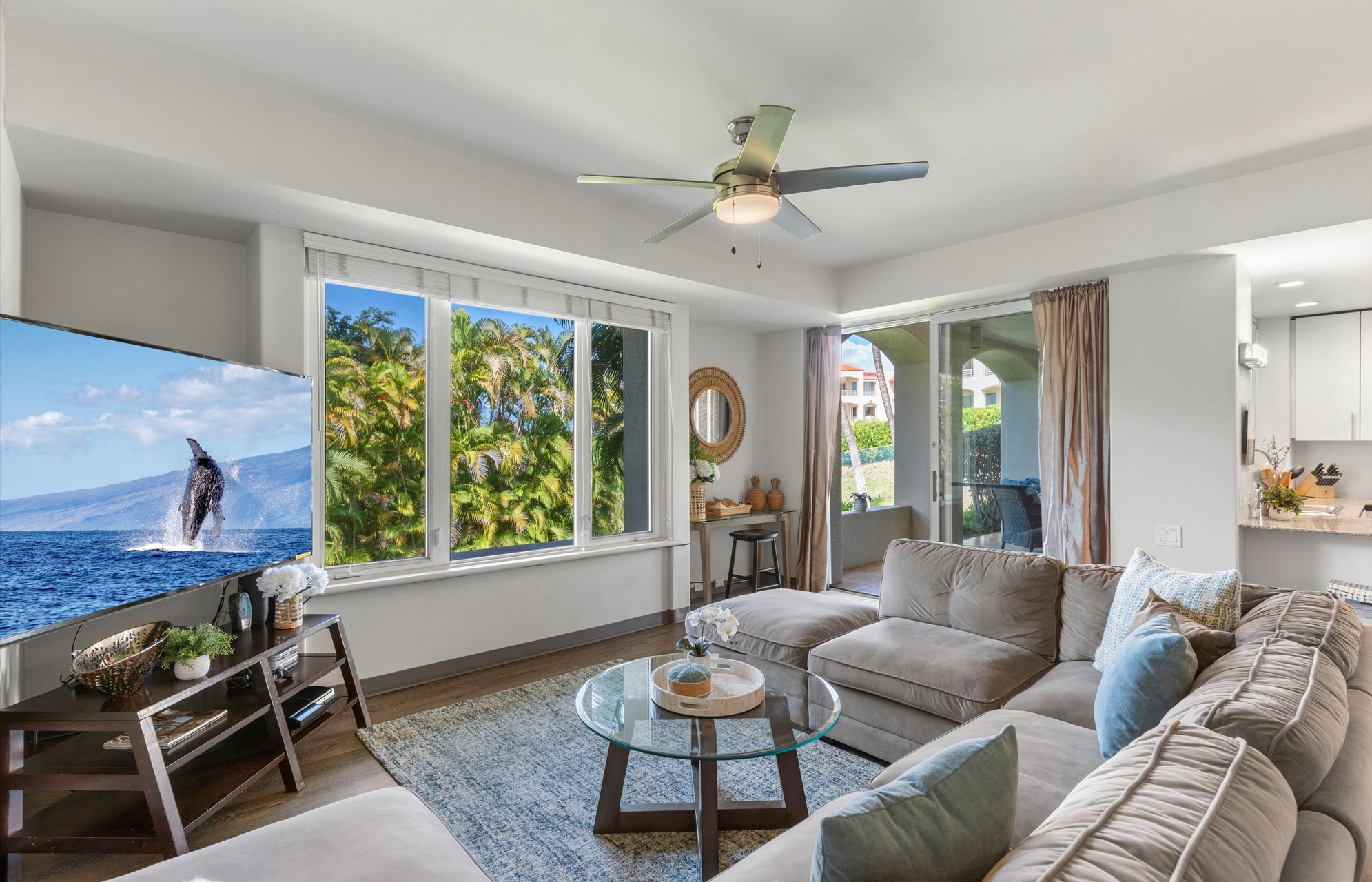 Step into your bright island retreat where soft ocean breezes and natural light fill the space through generous windows framing tropical palms. Sink into the plush sectional and unwind in your airy, breezy sanctuary.