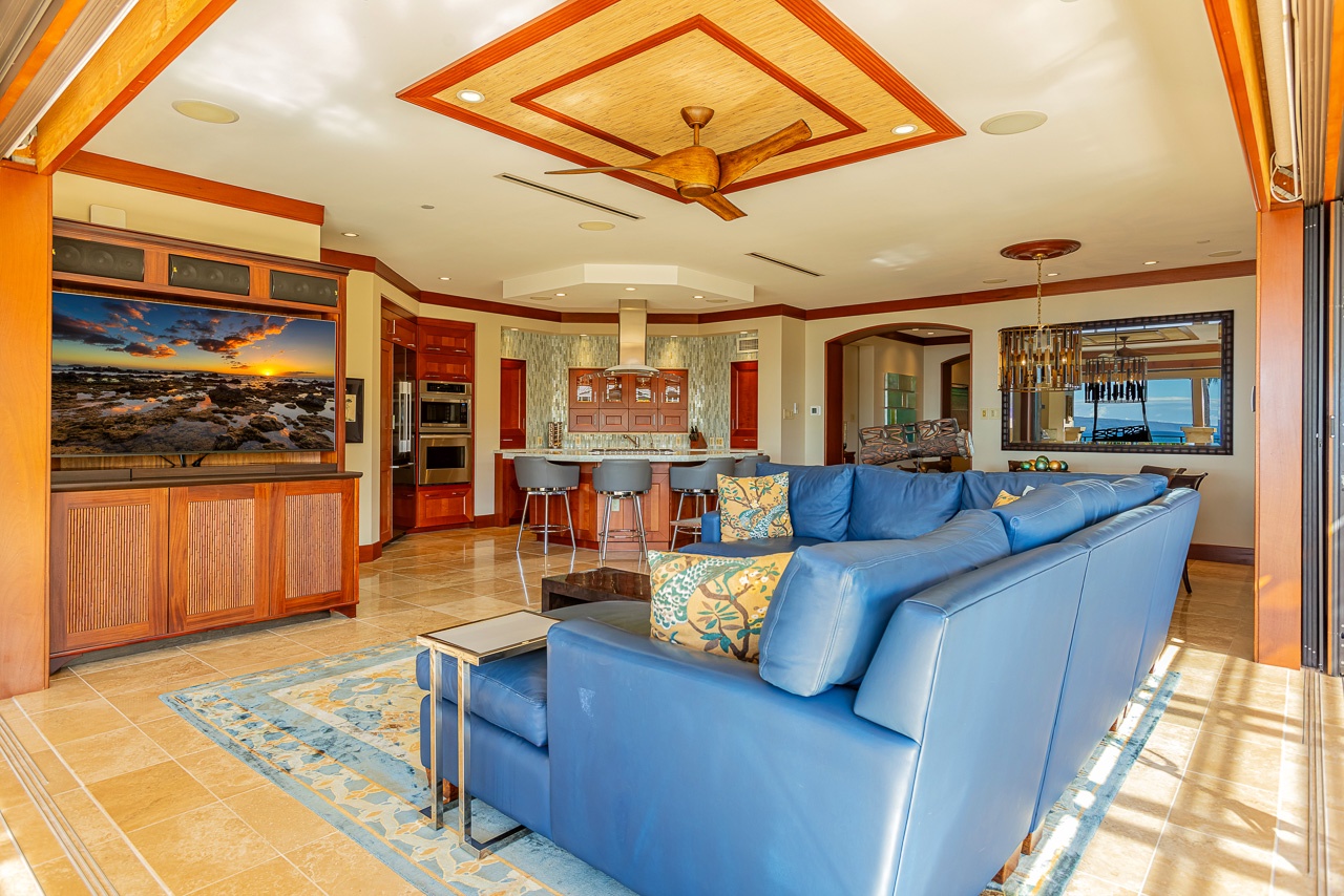 Sink into the plush sofa and savor the open-concept design where living, dining, and kitchen spaces blend effortlessly under warm wood tones and tropical breezes flowing in from outside.