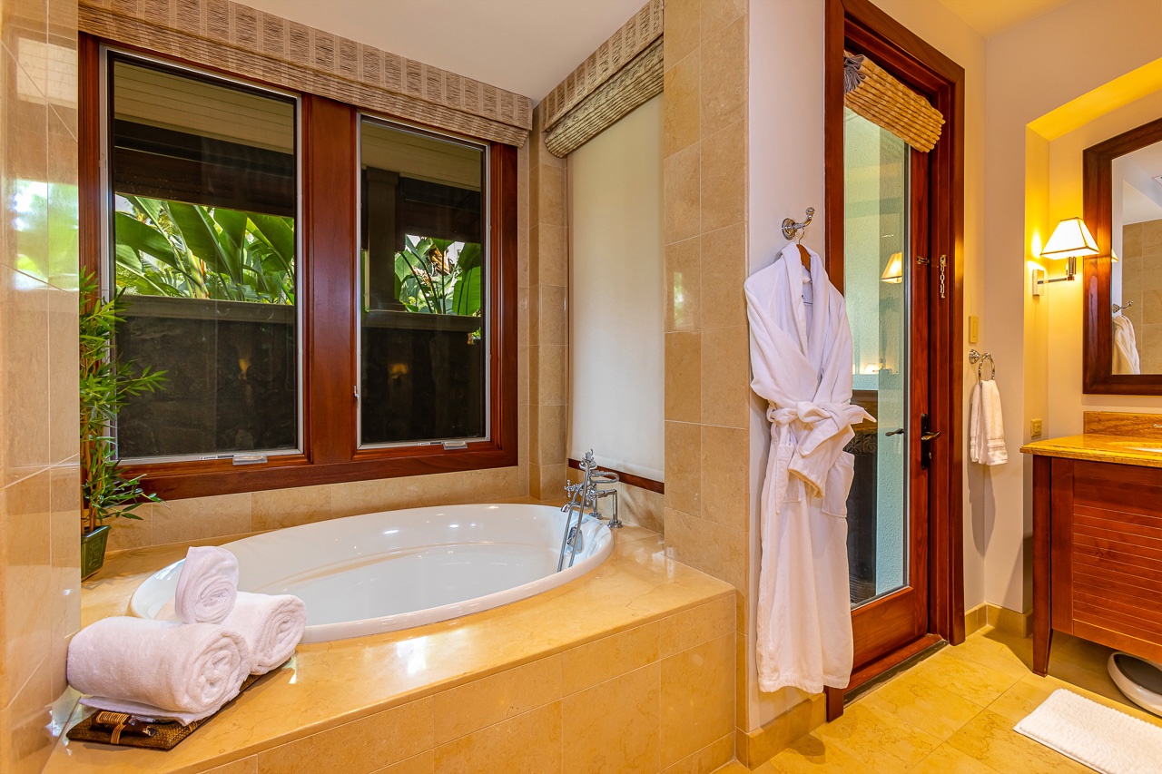 Slip into your robe and sink into a spa-inspired bathroom, where a soaking tub awaits beneath windows opening to lush tropical greenery, creating your private oasis for ultimate relaxation.