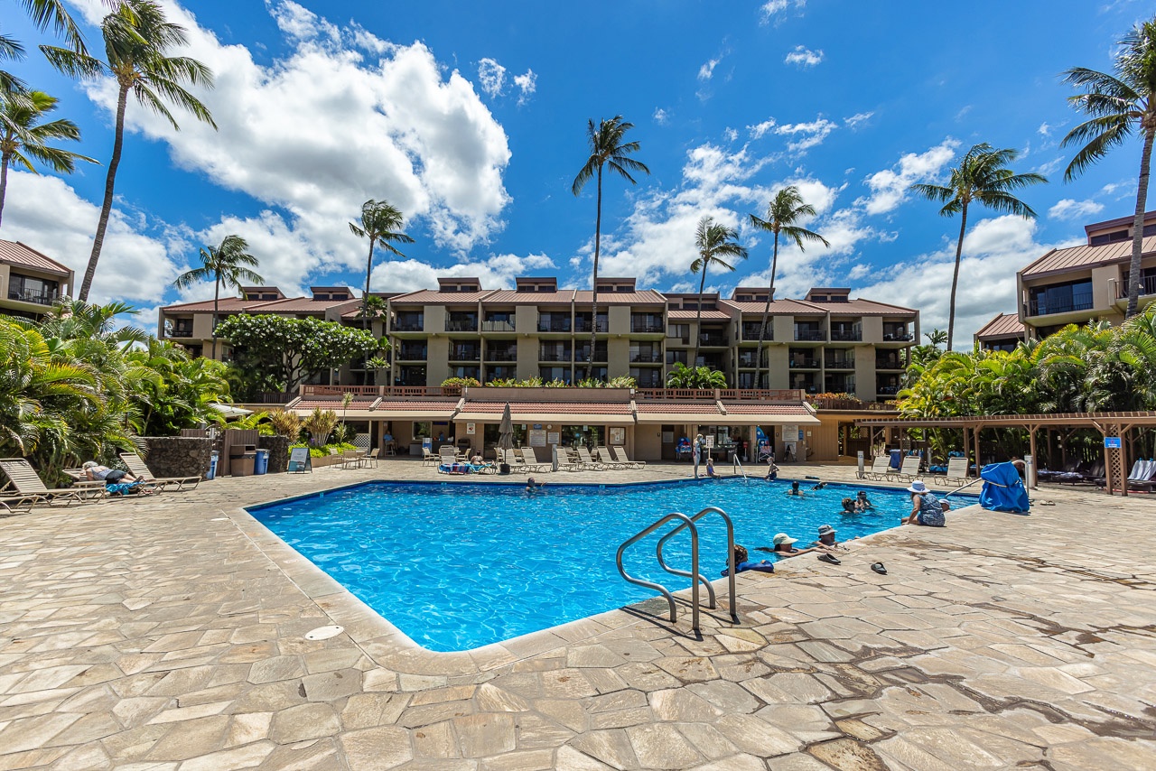 The property features a spacious swimming pool surrounded by tropical palms, with comfortable lounge seating and easy access to the main building—perfect for relaxing under the Hawaiian sun.