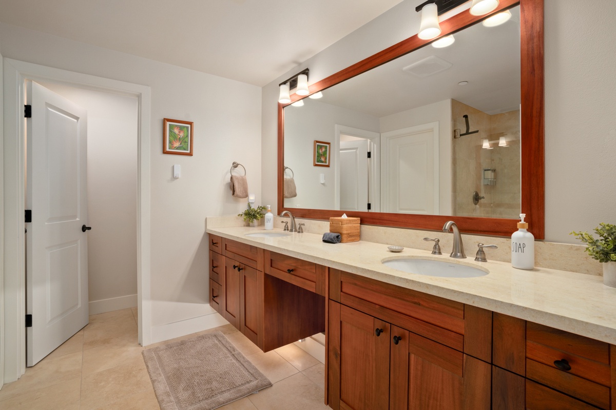 Your spacious primary bathroom features dual vanities with gleaming countertops and warm wood cabinetry, perfectly lit for your morning routine.