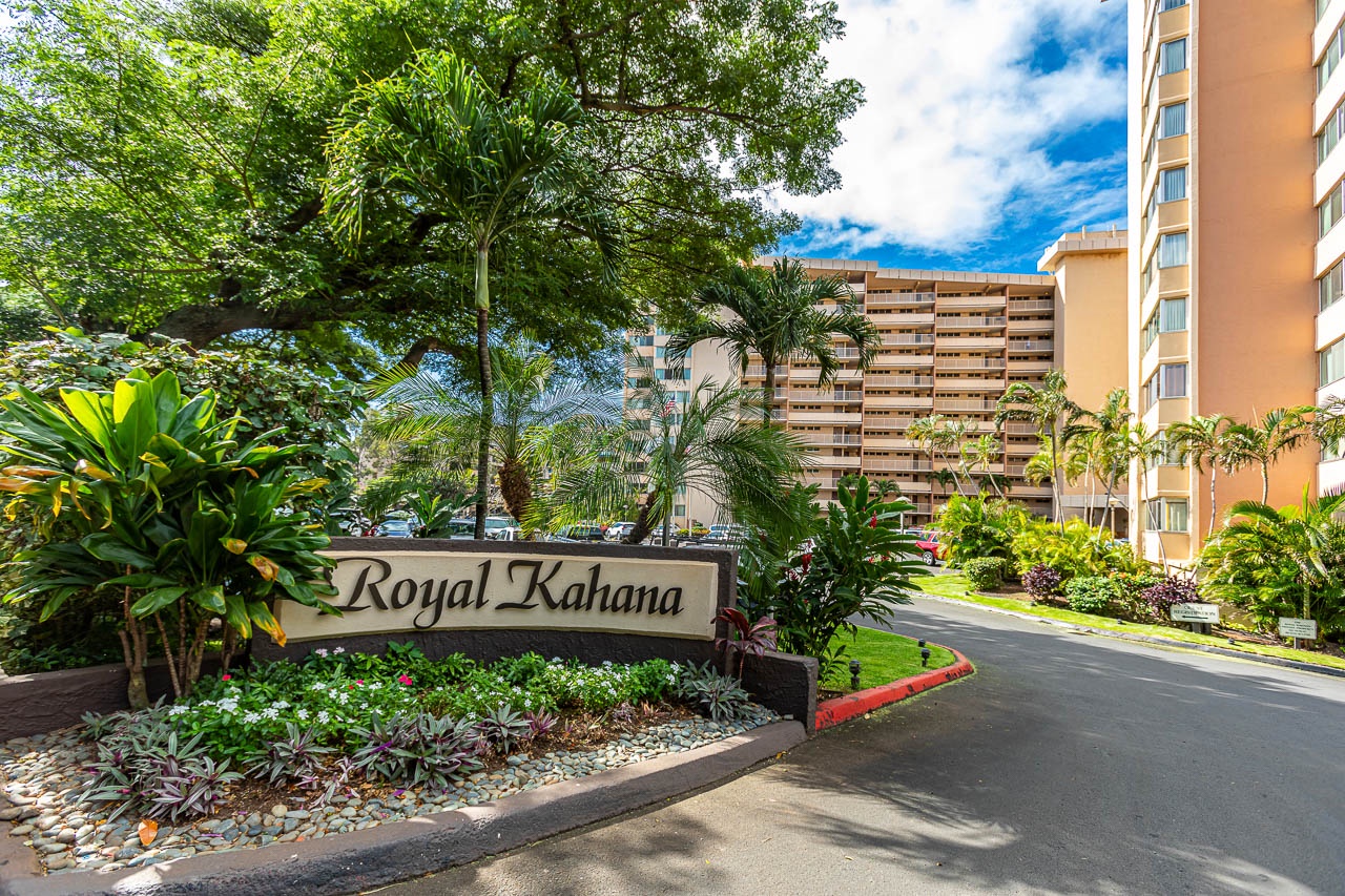 Entrance to Royal Kahana, surrounded by lush tropical landscaping and neighboring resort buildings, welcomes guests with vibrant greenery and island charm.