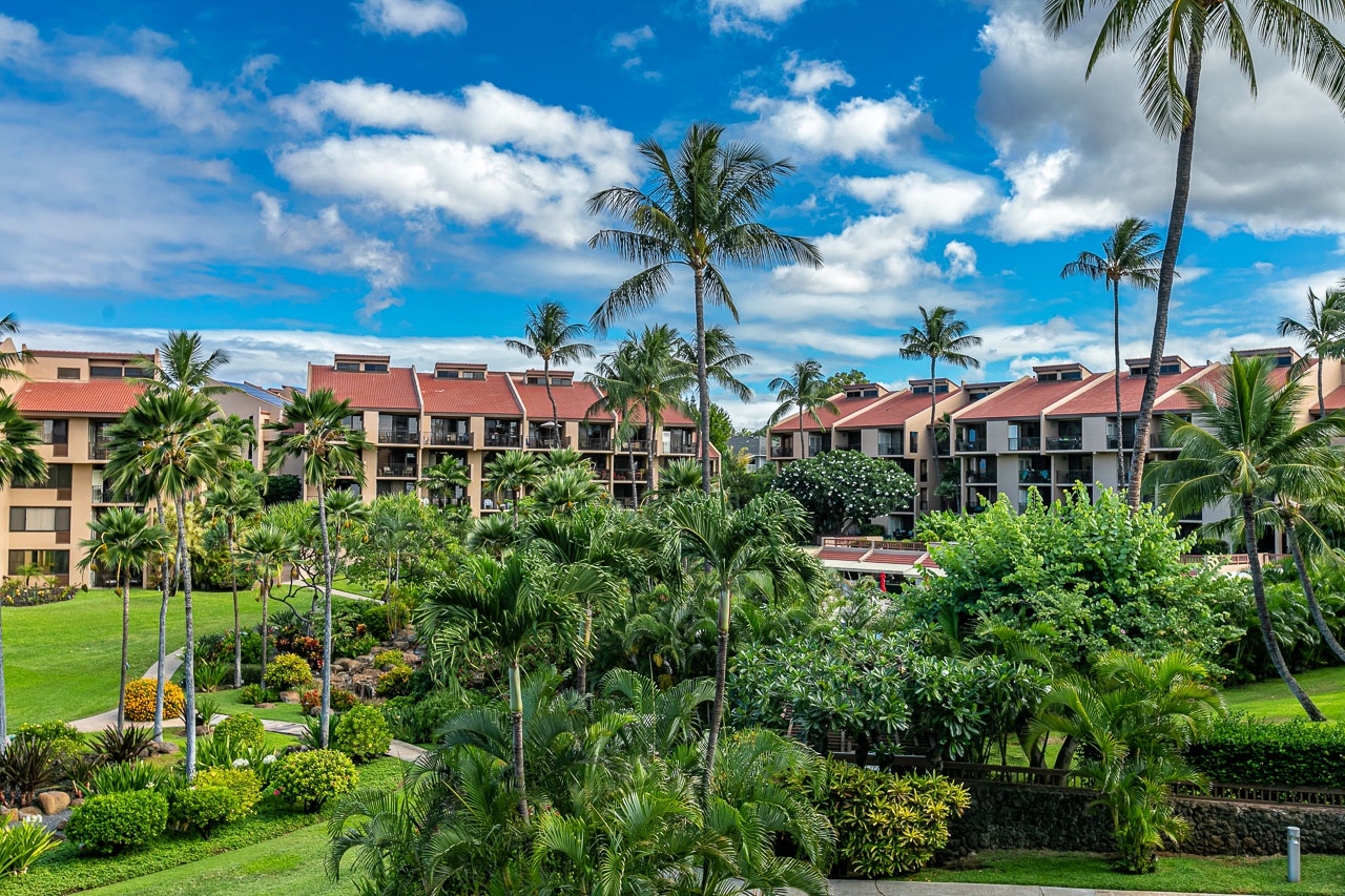 The property features multi-story buildings with distinctive red roofs set within beautifully landscaped tropical gardens complete with towering palms and vibrant greenery.