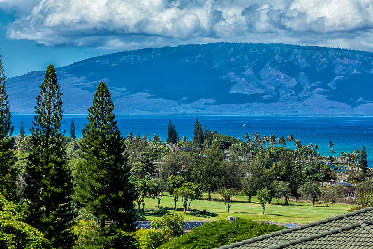 Elevated property location offering panoramic views of turquoise waters, dramatic mountain peaks, lush golf course greens, and tropical palm-lined coastline beneath expansive skies.
