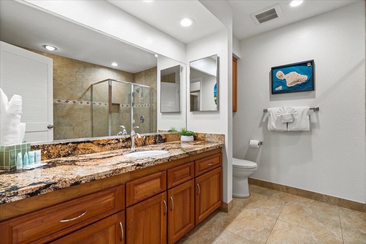 Your private bathroom features dual sinks with stunning granite countertops, a spacious glass-enclosed shower, and fresh towels artfully displayed for your comfort.