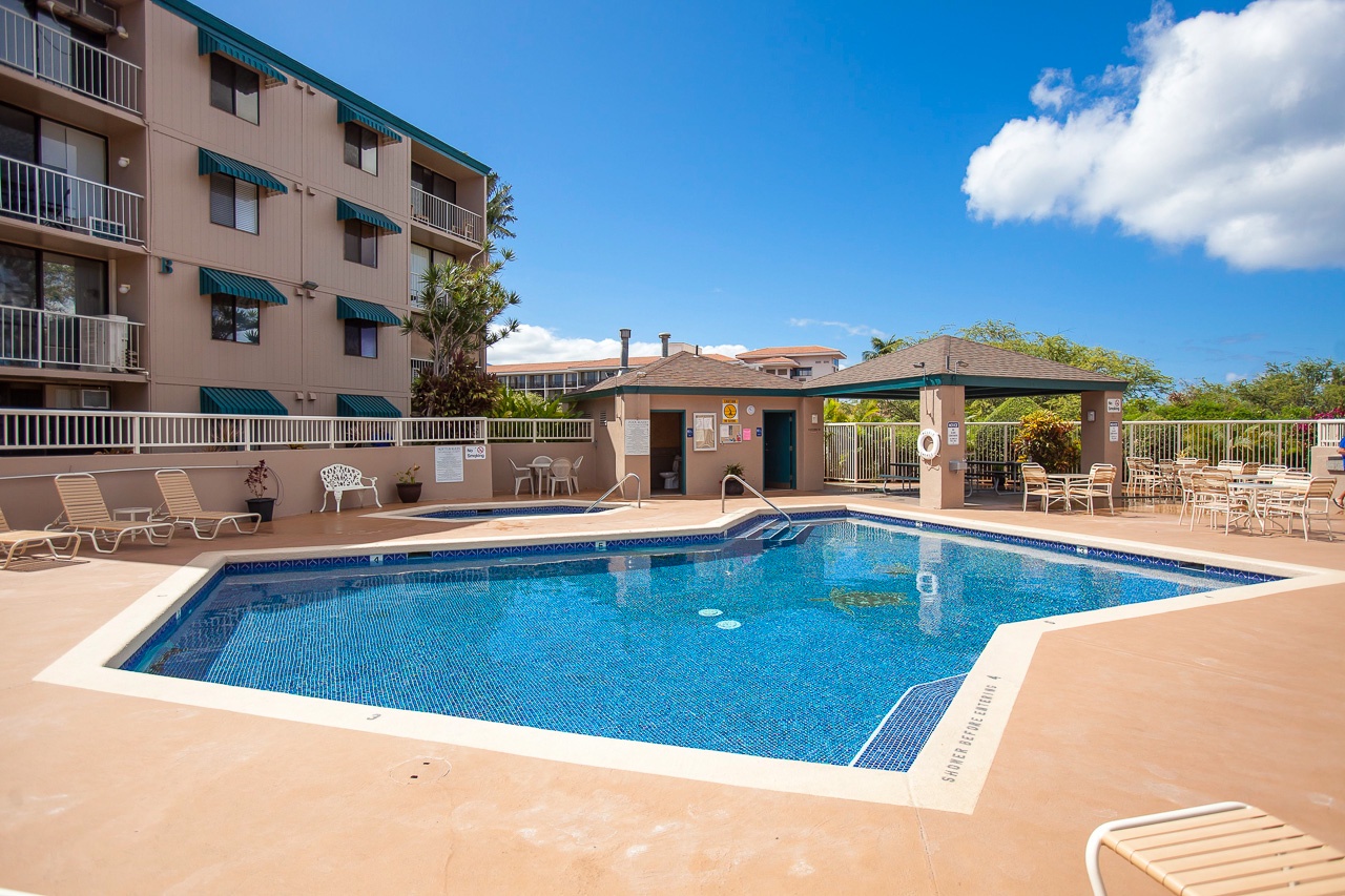 Sparkling community pool area surrounded by comfortable loungers and dining space under sunny blue skies.