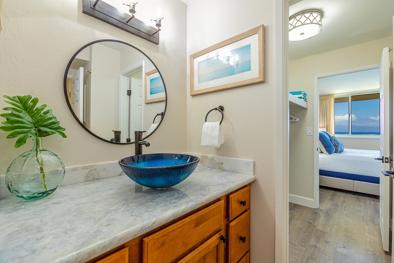 Step into your private bathroom, where a striking blue vessel sink and coastal art set a serene tone. Just beyond, your bedroom awaits with ocean views that invite you to unwind and truly escape.