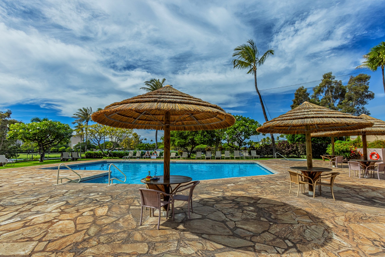 A tropical pool oasis awaits with thatched umbrellas, comfortable seating, and swaying palms under beautiful island skies—your perfect spot to unwind poolside.